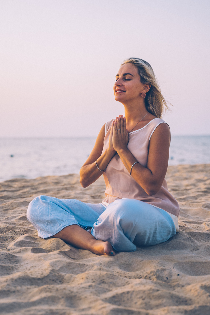 Woman in White Tank Top and Blue Denim Jeans Sitting on Beach Sand Doing Yoga